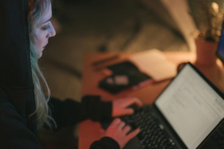 Woman focused on laptop work at a dimly lit desk.