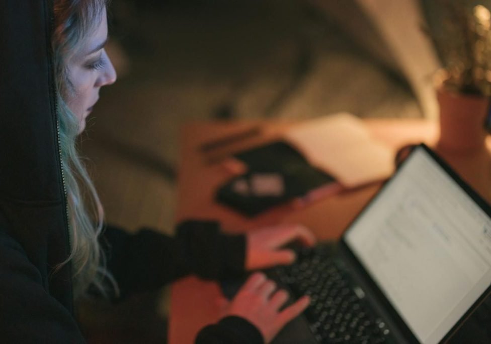 Woman focused on laptop work at a dimly lit desk.